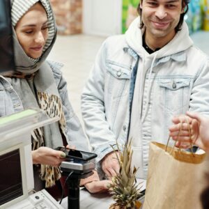 A smiling couple using a smartphone to pay at a supermarket checkout counter.